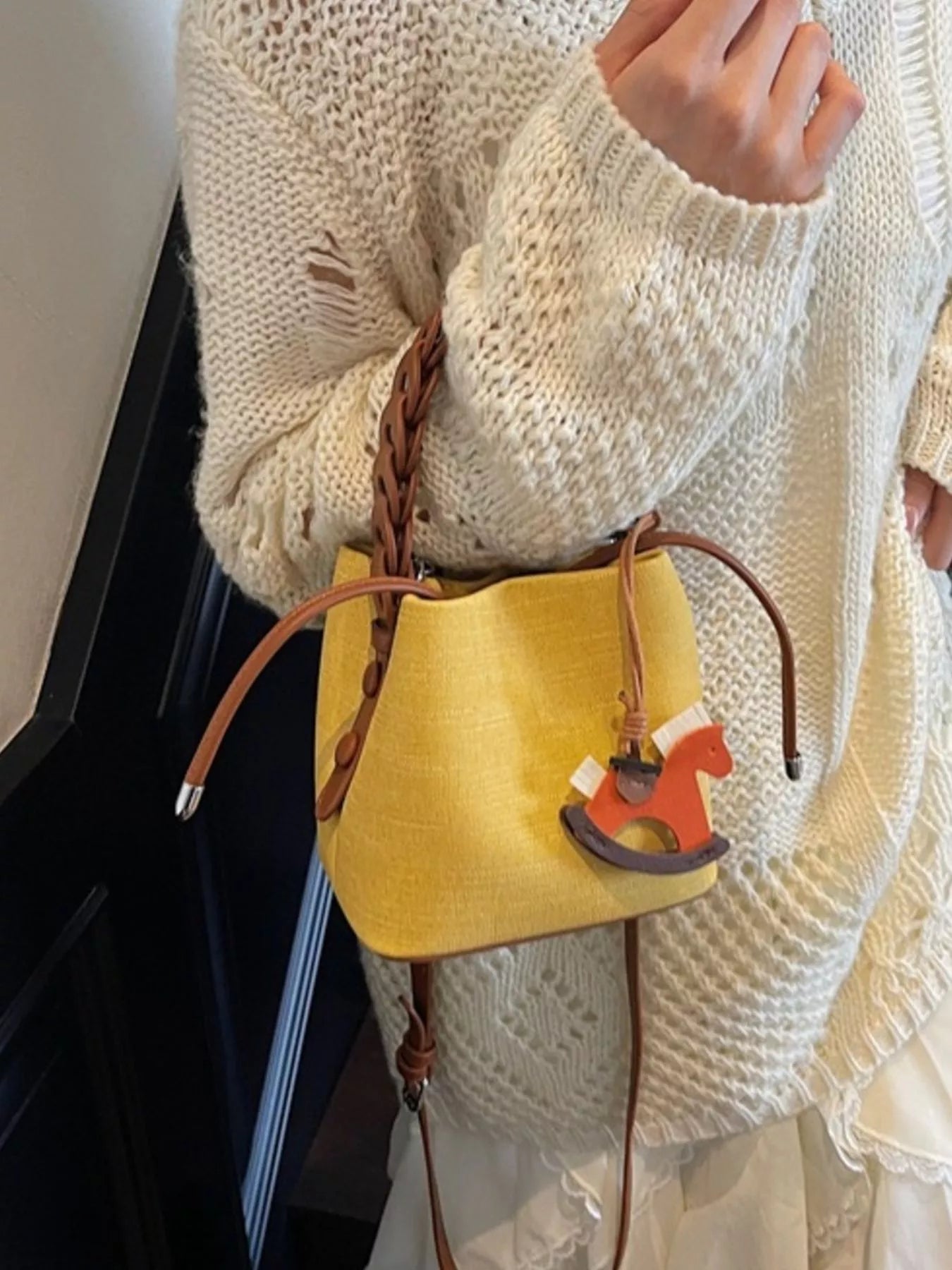 Yellow handbag with a horse charm held by a person wearing a white sweater.