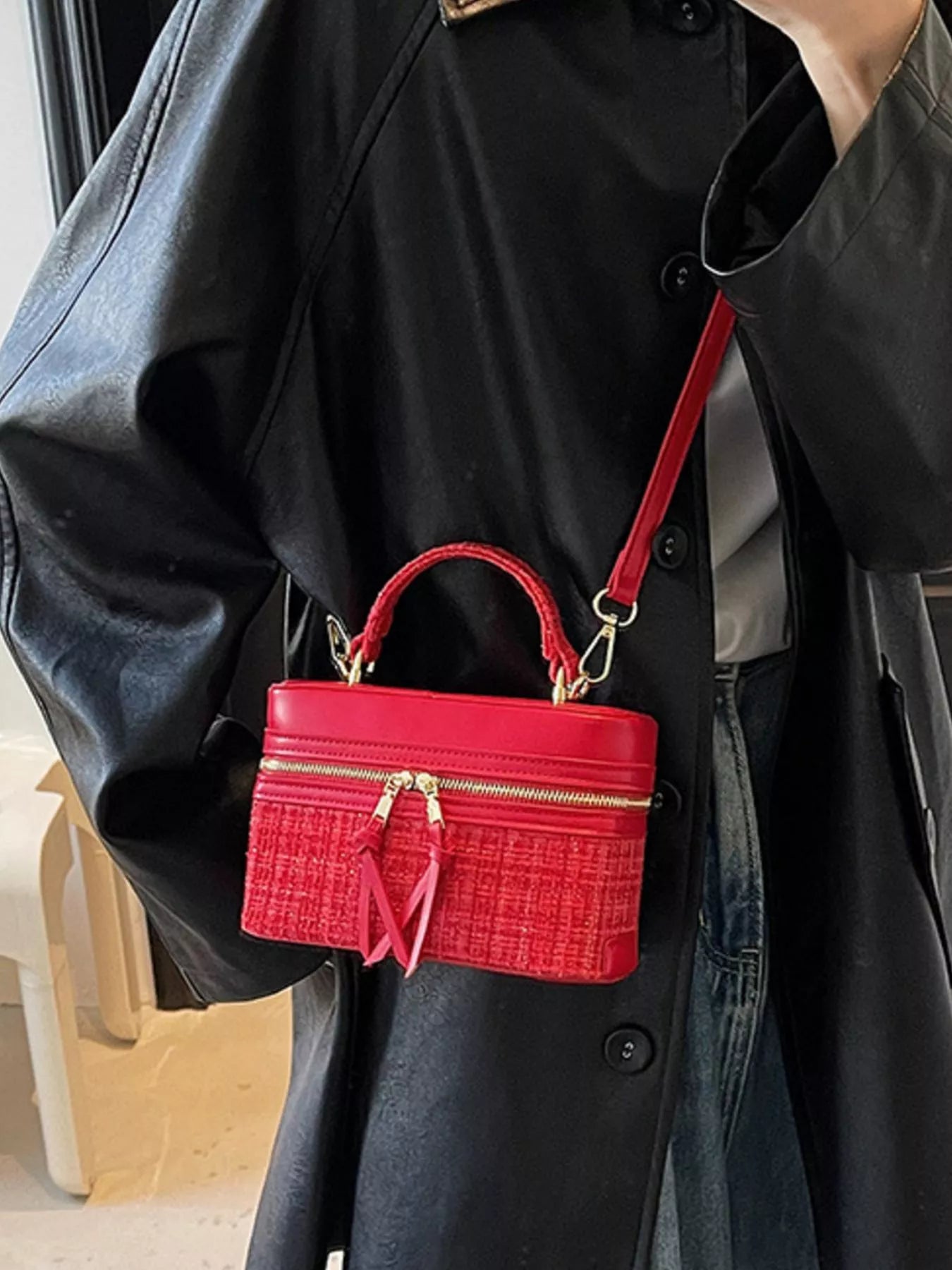 Red handbag with gold accents worn over a black coat
